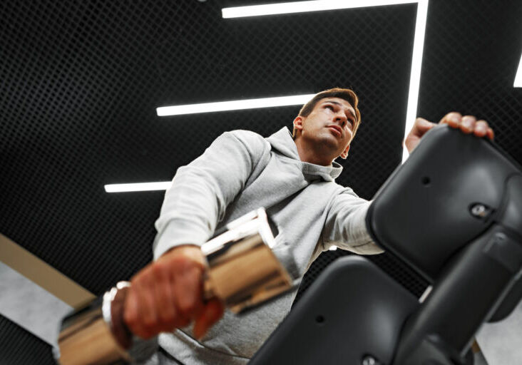 Determined handsome young male working out in gym with dumbbells