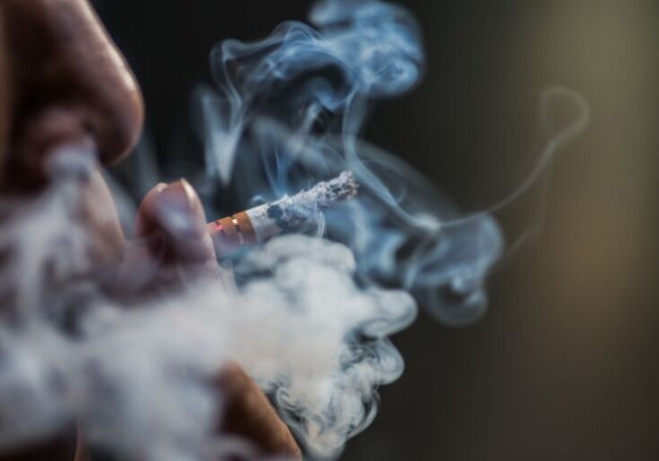 a closeup shot of a person puffing on a cigarette surrounded with smoke